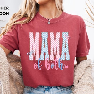 Könnte beinhalten: Weinrotes T-Shirt mit dem Text "MAMA of both" in einem rosa-blauen Karomuster. Das T-Shirt hat einen Rundhalsausschnitt und kurze Ärmel. Der Text "MAMA" ist in großen Buchstaben gehalten, mit "of both" in Schreibschrift.