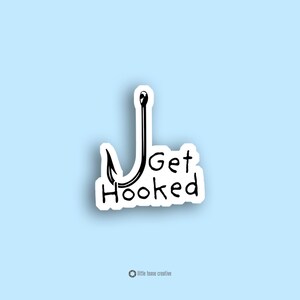 May include: A white sticker with a black fishing hook design and the words "Get Hooked" in a handwritten font. The sticker is on a light blue background. The words "little tease creative" are at the bottom.