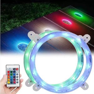 May include: Two illuminated LED rings with white mounting brackets. The rings are lit with blue and green lights. A remote control with multiple color options is held in a hand. The background shows a cornhole board with illuminated holes in red, green, and blue.