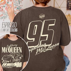 Op de afbeelding: Espresso-kleurig T-shirt met een groot wit nummer 95 op de rug en het opschrift "Lightning McQueen". De voorkant toont de tekst "Lightning McQueen" en een autografiek. Het shirt heeft ook de tekst "Think Fast".