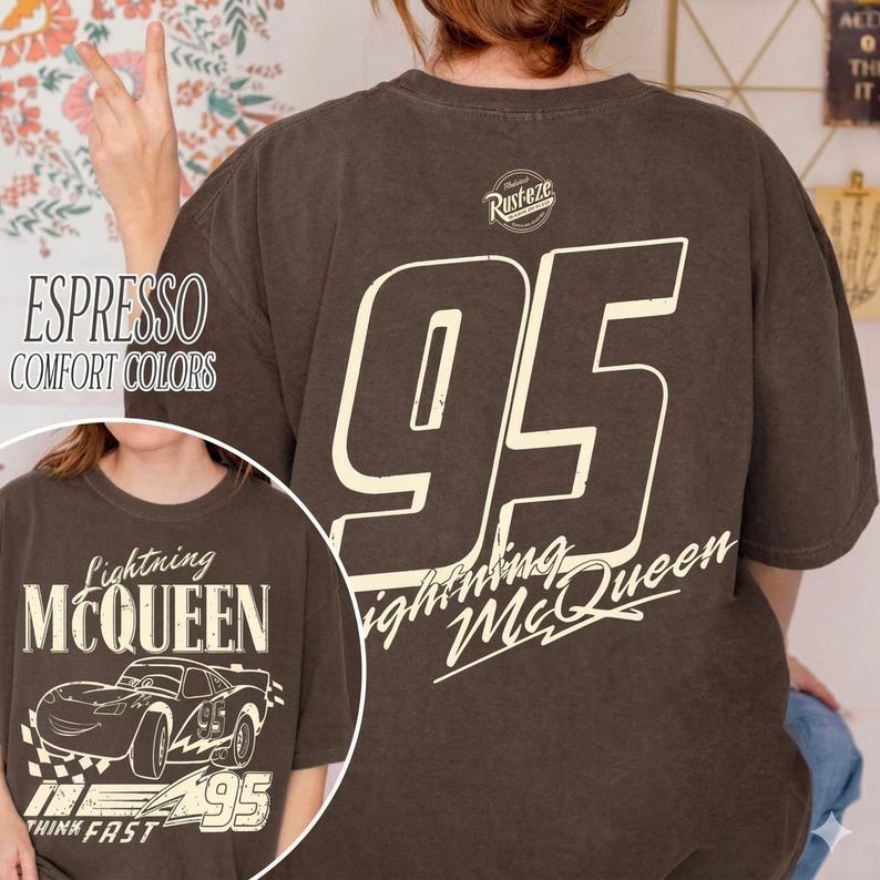 Op de afbeelding: Espresso-kleurig T-shirt met een groot wit nummer 95 op de rug en het opschrift "Lightning McQueen". De voorkant toont de tekst "Lightning McQueen" en een autografiek. Het shirt heeft ook de tekst "Think Fast".