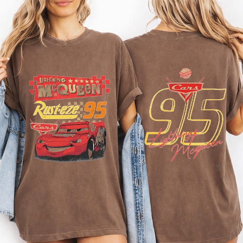 以下が含まれることがあります： 映画「カーズ」のライトニング・マックィーンが描かれた茶色のTシャツ。前面には「Lightning McQueen」、「Rusteze 95」、赤い車のイラスト。背面には黄色と赤で「95」と「Lightning McQueen」がデザインされています。映画をテーマにしたTシャツ。