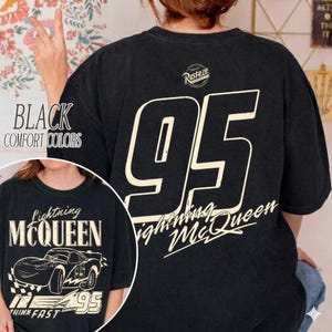 Op de afbeelding: Zwart T-shirt met het nummer 95 in grote letters op de rug. De voorkant toont een afbeelding van Lightning McQueen en de tekst "Lightning McQueen" en "Think Fast".