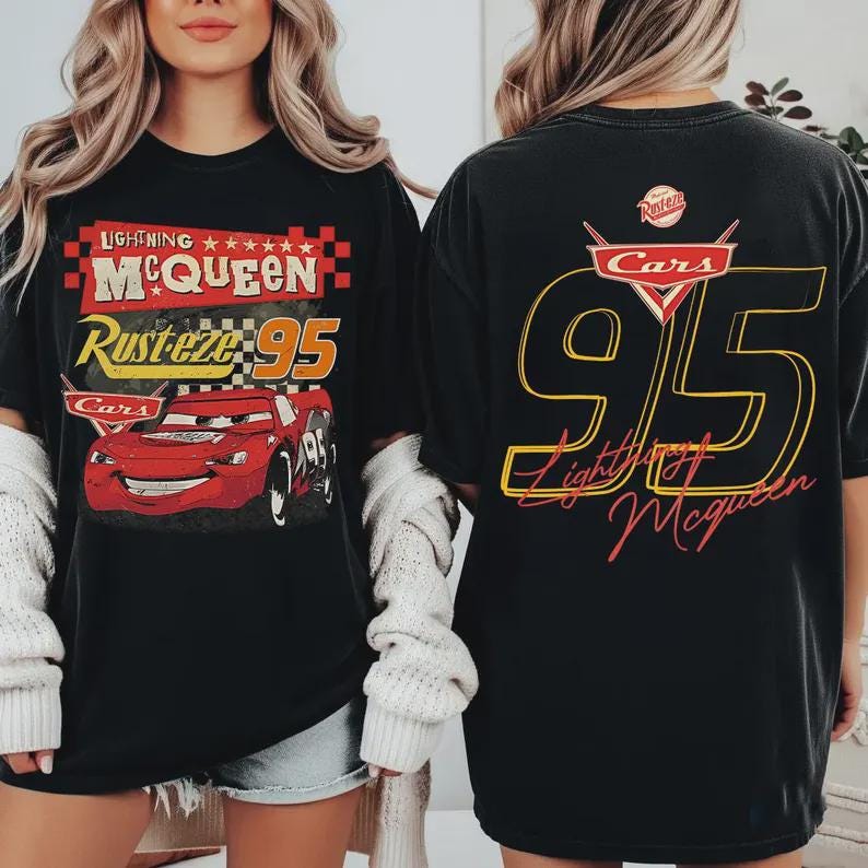 以下が含まれることがあります： 映画「カーズ」のライトニング・マックィーンが描かれた黒いTシャツ。前面には「Lightning McQueen」と「Rusteze 95」の文字と赤いレーシングカーのイラスト。背面には大きな「95」と「Lightning McQueen」が黄色と赤で描かれています。