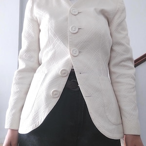May include: A white blazer with a diamond pattern and five buttons. The blazer has a slightly fitted silhouette and a curved hem.