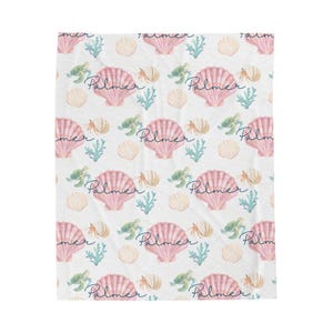 Peut inclure: Couverture blanche avec un motif répété de coquillages roses, de tortues de mer vertes et d'algues bleu-vert. Le nom "Palmer" est écrit en cursive. Une couverture douce et confortable.