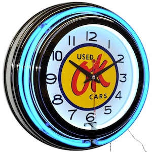 May include: A round, neon clock with a black and chrome frame. The clock face is white with black numerals and hands. The center features a yellow circle with the words "OK Cars" in red. A bright blue neon tube surrounds the clock face.