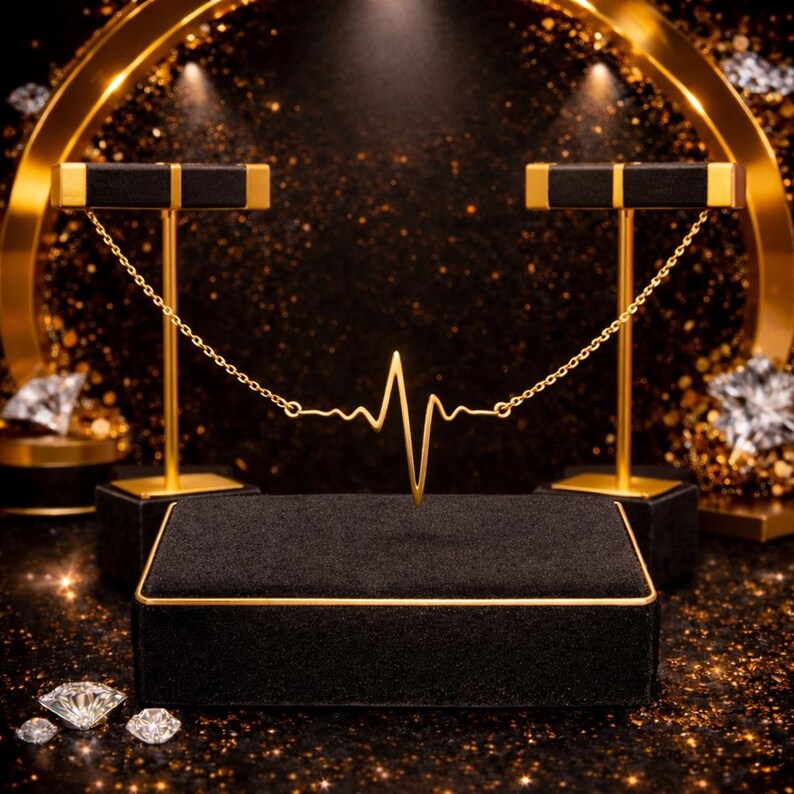 Peut inclure: Un collier en or en forme de battement de c&oelig;ur est pr&eacute;sent&eacute; sur un pr&eacute;sentoir &agrave; bijoux en velours noir avec des bordures dor&eacute;es. Deux supports dor&eacute;s avec des dessus noirs soutiennent la cha&icirc;ne du collier. Des diamants sont dispers&eacute;s.
