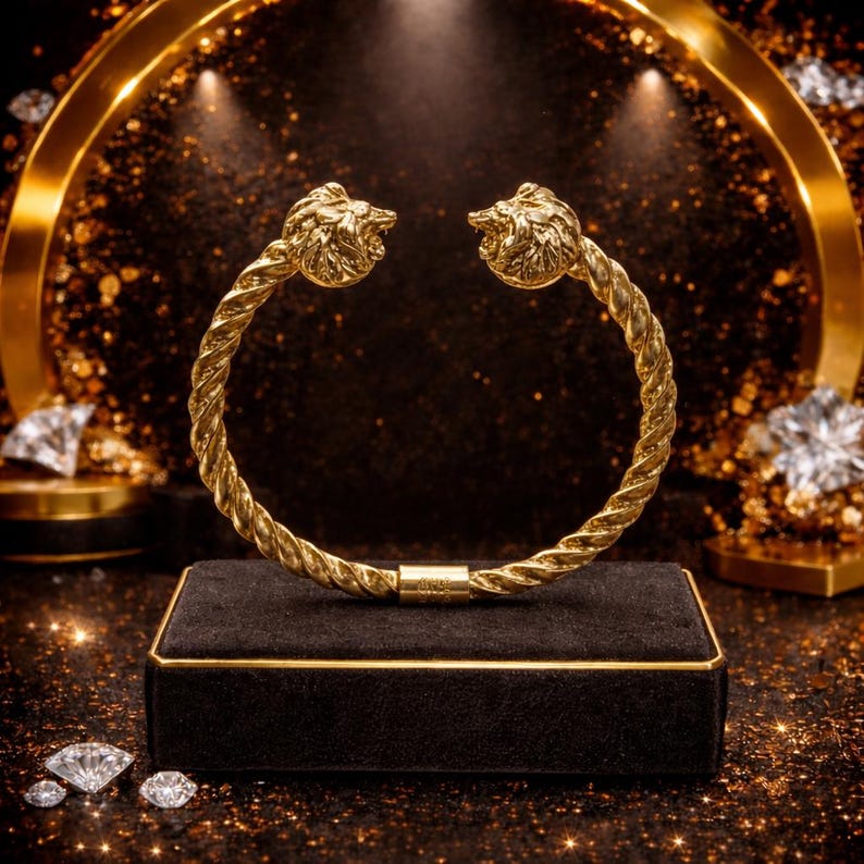Peut inclure: Un bracelet dor&eacute; avec un design torsad&eacute; en forme de corde. Le bracelet pr&eacute;sente des d&eacute;tails de t&ecirc;te de lion &agrave; chaque extr&eacute;mit&eacute;. Il est pr&eacute;sent&eacute; sur un coffret en velours noir avec des bordures dor&eacute;es, sur fond sombre avec des accents scintillants.