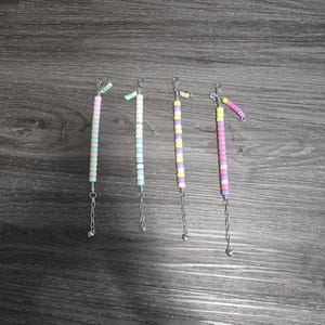以下が含まれることがあります： パステルカラーのビーズキーホルダーアクセサリー4点。各キーホルダーは、緑、白、青、紫、ピンク、黄色のビーズなど、異なる配色になっています。シルバーチェーンと、端に小さなチャームが付いています。