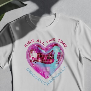 Puede incluir: Camiseta blanca con un diseño de bola de discoteca en forma de corazón. El corazón es rosa y azul con efecto espejo. El texto alrededor del corazón dice "KISS. ALL THE. TIME." y "DISCO.OCCASIONALLY."