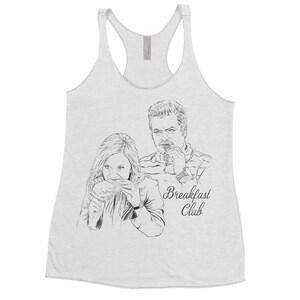 May include: A white tank top with a black and white illustration of two people eating. The text "Breakfast Club" is printed below the illustration.