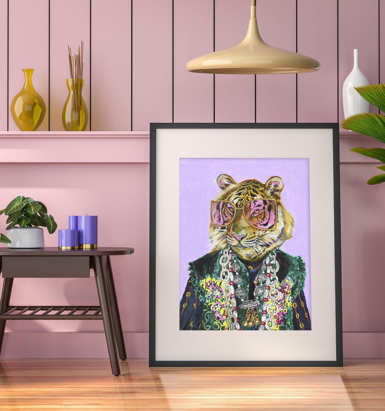 May include: A framed print of a tiger wearing pink sunglasses and a colorful beaded necklace. The tiger is depicted against a light purple background.