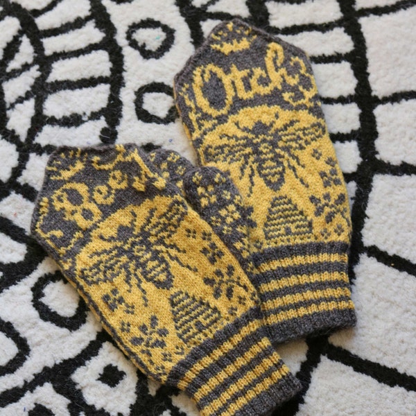 Peut inclure: Une paire de mitaines en tricot gris et jaune avec un motif d'abeille et de nid d'abeille. Les mitaines ont un poignet rayé.
