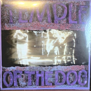 Può includere: Una copertina quadrata per disco in vinile con il testo TEMPLE OF THE DOG in lettere viola, testurizzate e in rilievo. Il centro contiene una fotografia in bianco e nero di una band sul palco, incorniciata da un bordo glitterato rosso scuro e viola.