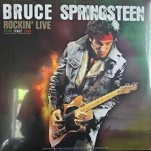 Puede incluir: Una portada de disco de vinilo con Bruce Springsteen tocando una guitarra eléctrica. El texto dice BRUCE SPRINGSTEEN ROCKIN' LIVE FROM ITALY 1993 LIVE RADIO BROADCAST. La imagen muestra a una persona con chaqueta de mezclilla y cinta roja.