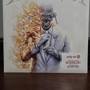 Könnte beinhalten: Albumcover der Band Megadeth. Das Artwork zeigt eine schädelgesichtige Figur im Anzug, mit Flammen auf der linken Seite. Der Text "MEGADETH" steht oben. Ein Aufkleber weist auf eine exklusive Vinyl mit den Titeln "BLOODLUST" und "BLOOD RED" hin.