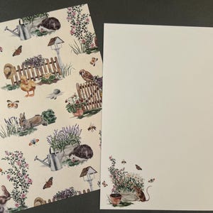 May include: Stationery set featuring a cream-colored paper with a garden-themed pattern. The pattern includes illustrations of a watering can, hedgehog, rabbit, butterflies, and flowers. A blank sheet of paper is also included.