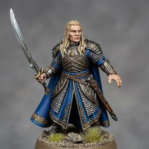 Puede incluir: Una figura miniatura pintada a mano de un guerrero con cabello largo rubio, vistiendo una armadura azul y plateada con detalles de filigrana dorada. La figura sostiene una espada plateada en la mano derecha, lleva una capa azul y una base.