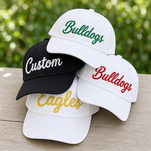 Puede incluir: Una colección de cuatro gorras de béisbol con texto bordado. Una gorra negra muestra la palabra Custom en blanco. Tres gorras blancas presentan texto bordado: Bulldogs en verde, Bulldogs en rojo y Eagles en amarillo.