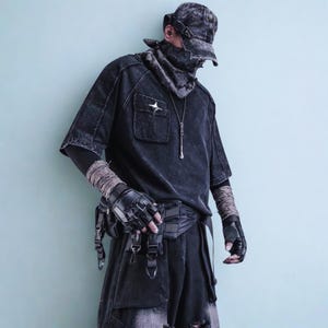 May include: A dark gray, distressed-wash outfit featuring a short-sleeved shirt with a chest pocket and a star emblem, paired with matching shorts. The ensemble includes a cap, neck covering, fingerless gloves, and a utility belt. A silver pendant hangs from the shirt.