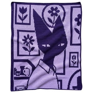 May include: A rectangular crochet blanket featuring a dark purple silhouette of a cat-like figure with pointed ears. The background is light purple and decorated with various framed floral patterns and simple line art of household objects.