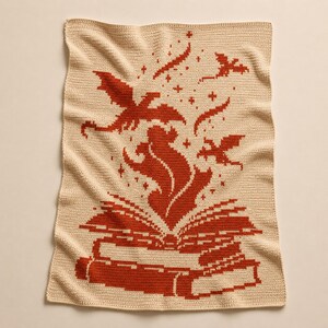 May include: A rectangular crochet blanket in cream with a rust-colored pattern. The design features an open book at the bottom with flames rising from the pages, surrounded by small stars and two flying dragon silhouettes above the flames.