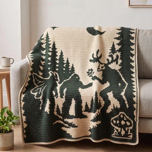 Può includere: Una coperta all'uncinetto color crema e verde scuro che raffigura una scena boschiva con una grande creatura, un alce e un fungo. Il design include alti pini e una luna crescente, con un bordo verde scuro che incornicia tutto il tessuto.