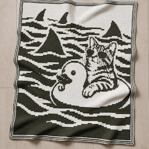 May include: A rectangular crochet blanket featuring a dark green and white pixelated design. The pattern depicts a cat wearing sunglasses floating on a duck-shaped pool float in water with several shark fins visible in the background.