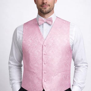 May include: A light pink paisley patterned vest and matching bow tie. The vest has a button-up front and two front pockets. The outfit is worn over a white dress shirt and black pants. Formal wear.