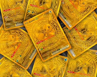 May include: A collection of gold-colored trading cards featuring various cartoon characters. The cards have intricate designs and text, with the central card showcasing a character named Eevee. The cards are arranged on a dark surface.