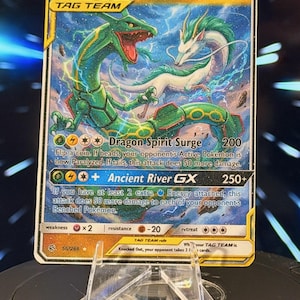 K&ouml;nnte beinhalten: Eine Rayquaza & Haku GX Tag Team Sammelkarte. Die Karte zeigt eine gr&uuml;ne und wei&szlig;e Drachenillustration mit dem Text "Dragon Spirit Surge" und "Ancient River GX". Die Karte wird auf einem transparenten Kunststoffst&auml;nder pr&auml;sentiert.