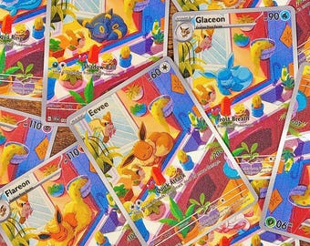 Könnte beinhalten: Eine Sammlung von Pokémon-Sammelkarten mit Charakteren wie Eevee, Flareon und Glaceon. Die Karten zeigen farbenfrohe Illustrationen und Texte, die Angriffe und Fähigkeiten beschreiben. Die Karten sind verstreut, um ihre Designs zu präsentieren.