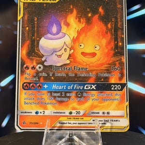 K&ouml;nnte beinhalten: Eine Pok&eacute;mon-Sammelkarte mit Litwick und Calcifer GX. Die Karte hat einen goldenen Rand und zeigt eine kerzenartige Kreatur und einen feurigen Charakter vor einem feurigen Hintergrund. Der Text enth&auml;lt "TAG TEAM" und Angriffsdetails.