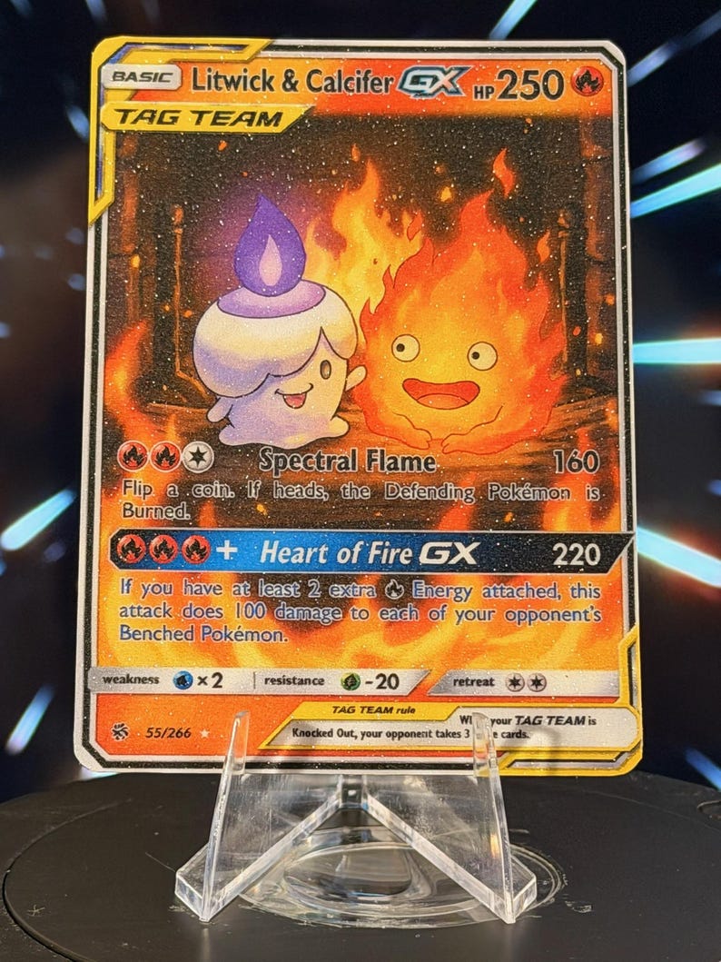 K&ouml;nnte beinhalten: Eine Pok&eacute;mon-Sammelkarte mit Litwick und Calcifer GX. Die Karte hat einen goldenen Rand und zeigt eine kerzenartige Kreatur und einen feurigen Charakter vor einem feurigen Hintergrund. Der Text enth&auml;lt "TAG TEAM" und Angriffsdetails.