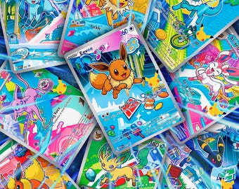 Könnte beinhalten: Eine Sammlung farbenfroher Sammelkarten mit verschiedenen Zeichentrickfiguren. Die Karten haben einen silbernen Rand und zeigen Bilder von Kreaturen mit verschiedenen Fähigkeiten und Namen wie "Eevee", "Vaporeon" und "Sylveon". Die Karten liegen auf blauem Grund.