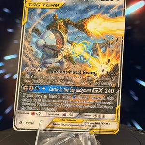 K&ouml;nnte beinhalten: Eine Pok&eacute;mon-Sammelkarte mit Registeel & Laputa Robot GX. Die Karte zeigt eine futuristische Kampfszene mit zwei Robotern und den Texten "Ancient Metal Beam" und "Castle in the Sky Judgment GX". Die Karte wird auf einem transparenten Kunststoffst&auml;nder pr&auml;sentiert.