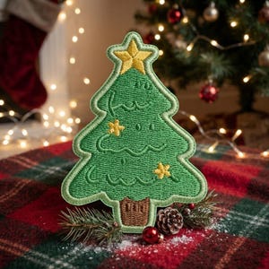 May include: An embroidered patch shaped like a green Christmas tree with a brown trunk and a yellow star at the top. The tree features stitched yellow star accents and wavy lines across its surface, with a thick green border outlining the shape.