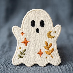 May include: An embroidered iron-on patch shaped like a ghost in off-white thread. The ghost features black stitched eyes and a mouth, accented with orange stars, a golden crescent moon, and small green and gold botanical leaf sprigs.