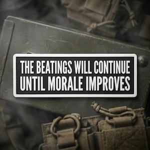 May include: A rectangular black and white patch with the text "THE BEATINGS WILL CONTINUE UNTIL MORALE IMPROVES." The patch is set against a backdrop of military gear, including a green metal container and tactical equipment.