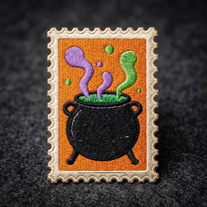 May include: A rectangular embroidered patch shaped like a postage stamp with a scalloped border. The design features a black cauldron on an orange background, with purple and green steam rising from the top and small green dots floating around.
