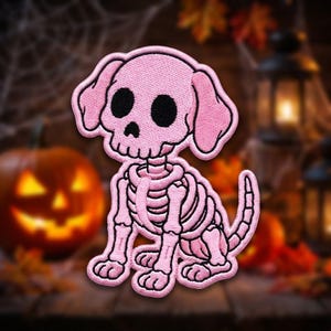 May include: An embroidered patch featuring a stylized dog skeleton in light pink thread with black eye sockets and a black nose. The design depicts a seated canine with floppy ears, a rib cage, and a tail, all outlined in a dark pink border.