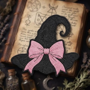 May include: A black embroidered patch shaped like a pointed hat with a curved tip. The hat features a large, light pink bow centered on the front. The embroidery consists of dense black thread for the hat and soft pink thread for the bow detail.