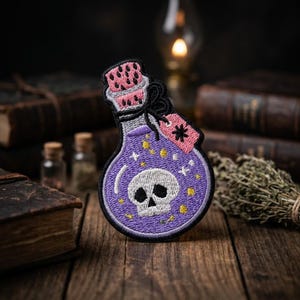May include: An embroidered patch shaped like a potion bottle with a purple liquid interior, a white skull graphic, and small yellow stars. The bottle has a pink cork, a black bow, and a small pink rectangular tag featuring a black asterisk symbol.