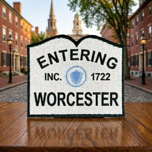 May include: A white embroidered patch with a black border featuring the text ENTERING, INC. 1722, and WORCESTER in black thread. A light blue circular emblem with a central shield design is positioned between the text INC. and 1722.