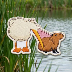 May include: An embroidered patch featuring a white pelican with an orange beak and feet, holding a brown capybara with black feet in its pink-lined beak. The patch has a white border and is shaped to follow the outlines of the two animals.