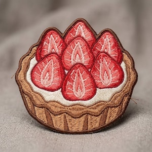 May include: An embroidered patch shaped like a fruit tart. The design features a brown crust, a layer of white cream, and five red strawberry slices arranged on top. The embroidery uses shades of red, pink, white, and brown thread throughout.