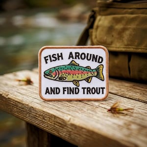 May include: A rectangular embroidered patch with a white background and a brown border. The patch features a colorful trout illustration in the center with the black text FISH AROUND above and AND FIND TROUT below the fish graphic.