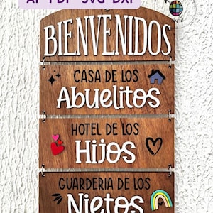 Könnte beinhalten: Willkommensschild aus Holz mit dem Wort "BIENVENIDOS" oben. Darunter stehen die Sätze "CASA DE LOS Abuelitos", "HOTEL DE LOS Hijos" und "GUARDERIA DE LOS Nietos". Das Schild enthält dekorative Elemente wie Herzen, ein Haus und einen Regenbogen.