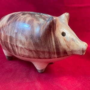 Puede incluir: Una alcancía de cerámica con esmalte marrón y blanco. La alcancía tiene un pequeño agujero en el lateral para monedas.